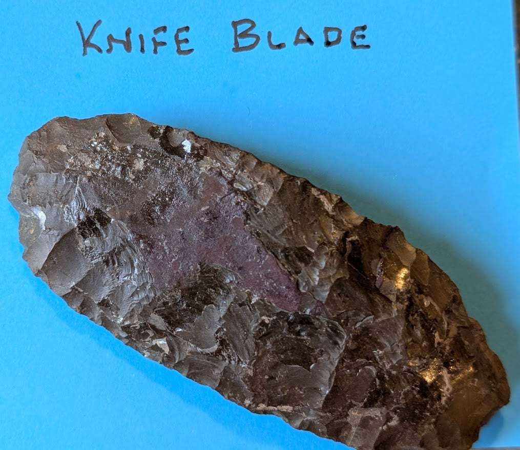 Large Native American flint knife blade with red quartz inclusion on blue background