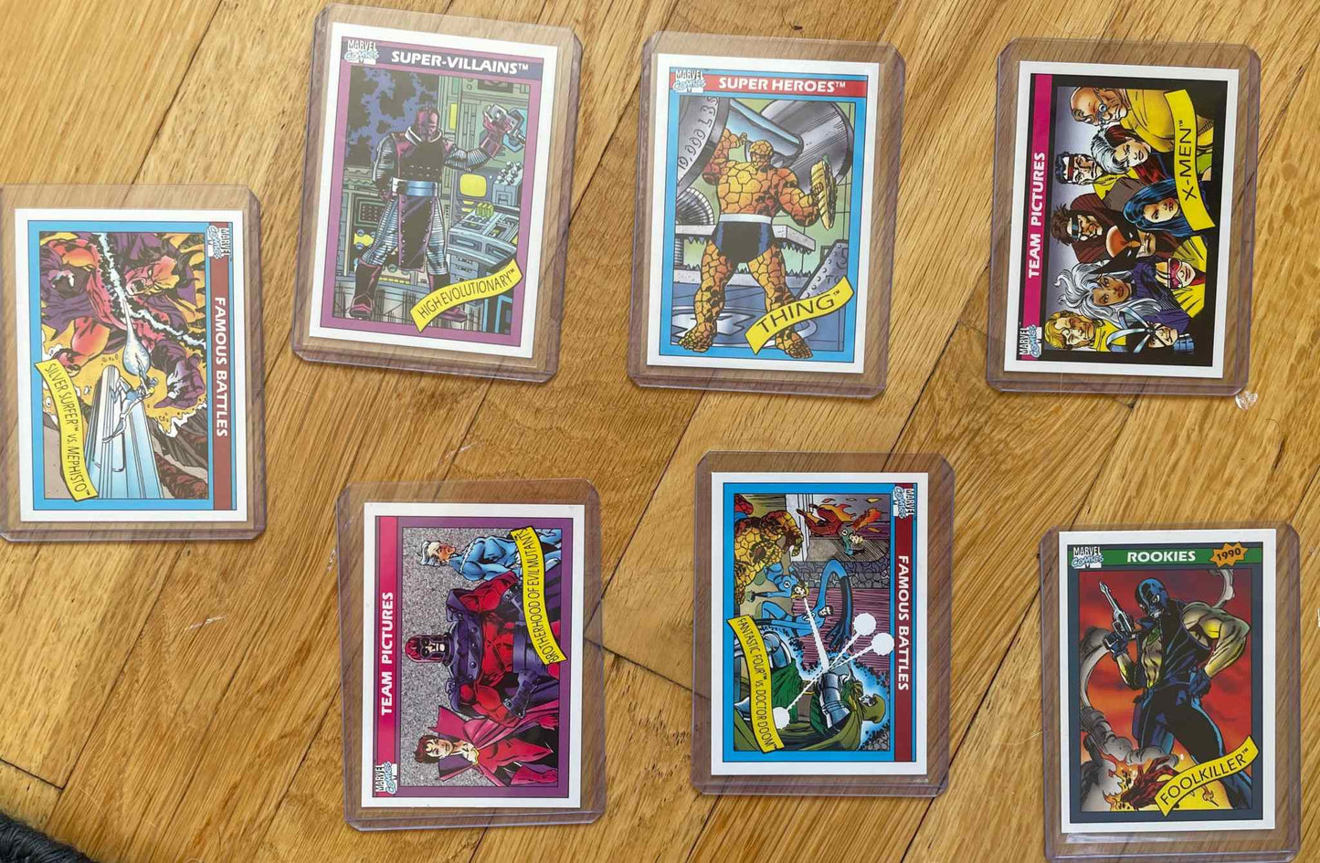 MINT/NM 1990 Marvel Universe Series 1 card lot featuring seven collectible cards displayed on a wooden surface.