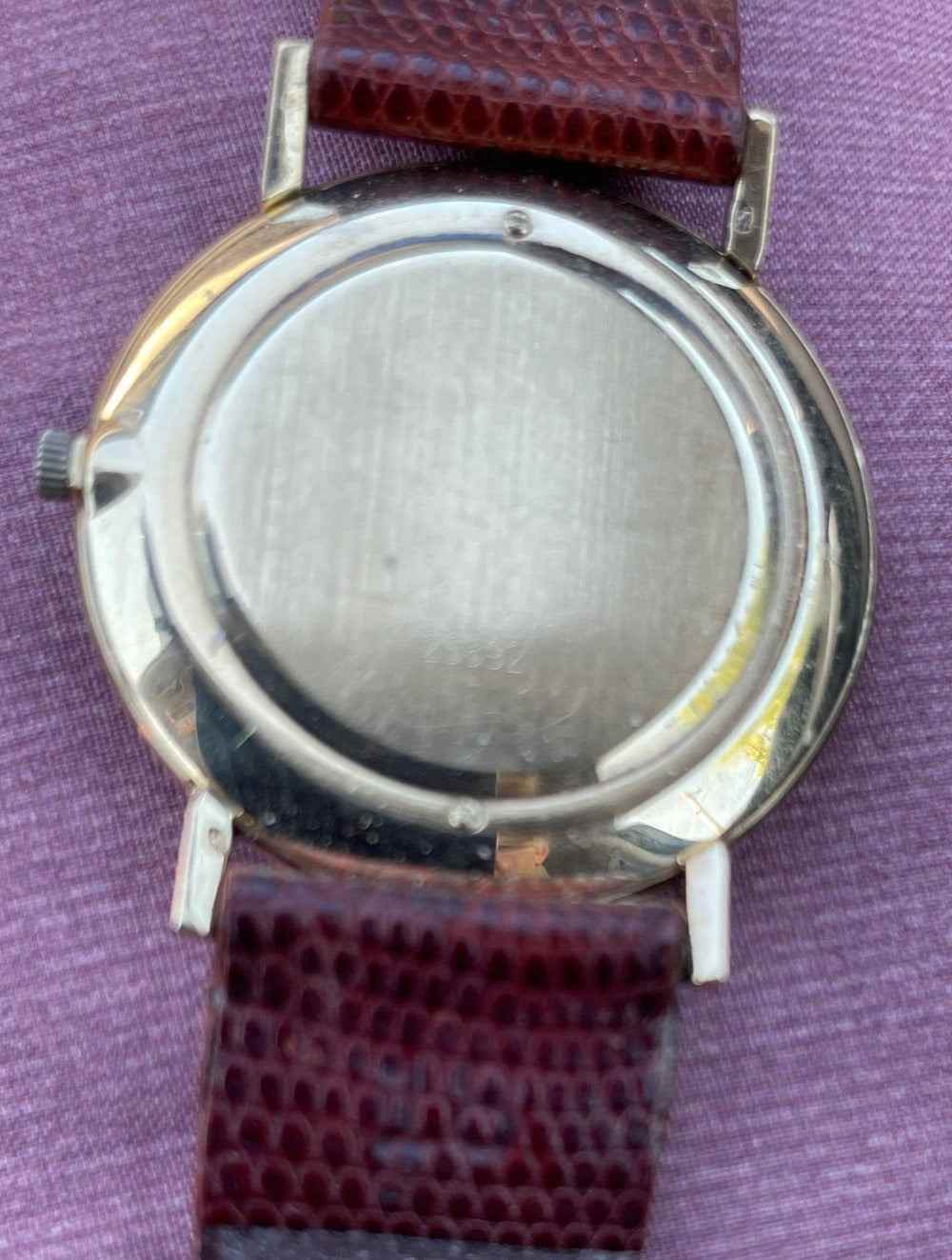 Vintage Lucien Piccard ultra slim 14k gold mechanical watch with leather strap on purple background.