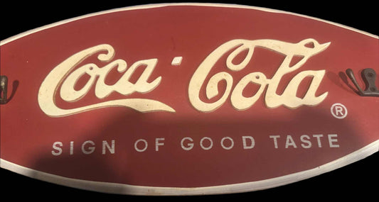 Coca-Cola wooden wall plaque with "Sign of Good Taste" text and hooks for hanging keys or accessories, vintage style 19x8 inches.