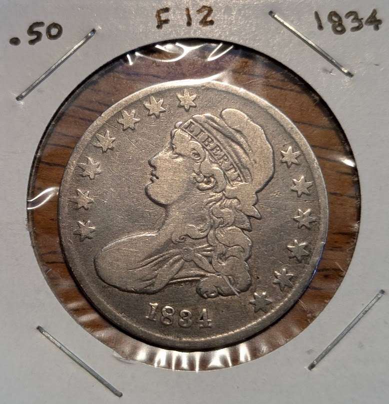 1834 Capped Bust Half Dollar silver coin with a worn, gray-toned surface, Liberty portrait, and surrounding stars in a holder.