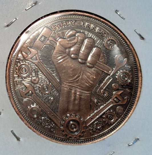 Dirty Hands side of antiqued copper round showing a clenched fist, tools and gears